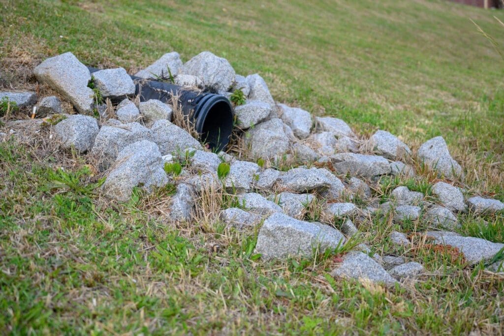 A black pipe rests in the grass beside several rocks creating a natural outdoor scene