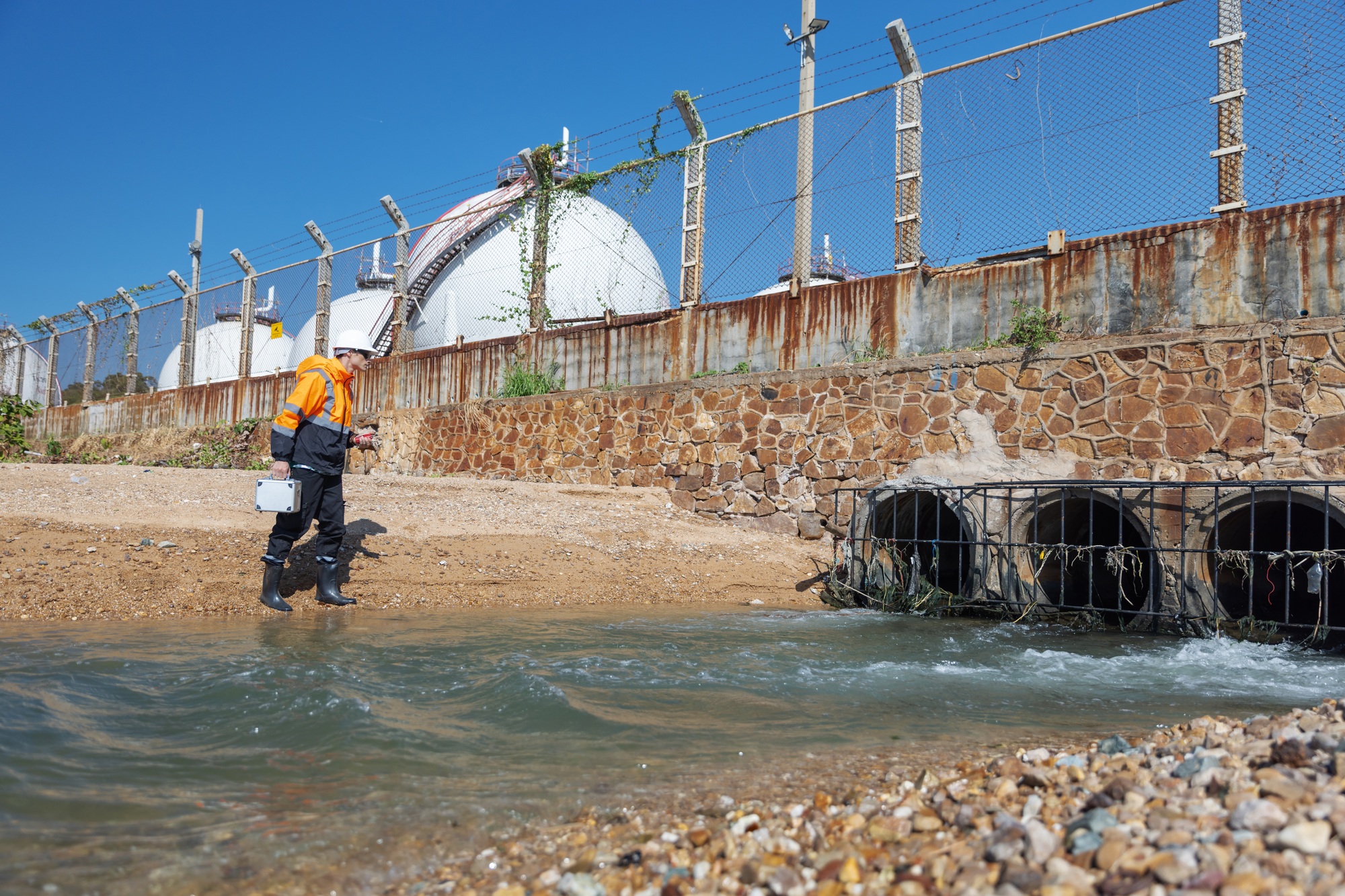 An environmental engineer inspects water flow near an industrial drainage outlet.