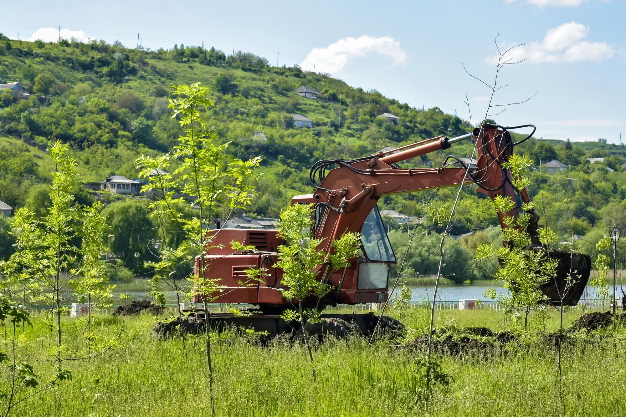 Construction machinery at Work. Red excavator digs into the earth on a lush green hillside