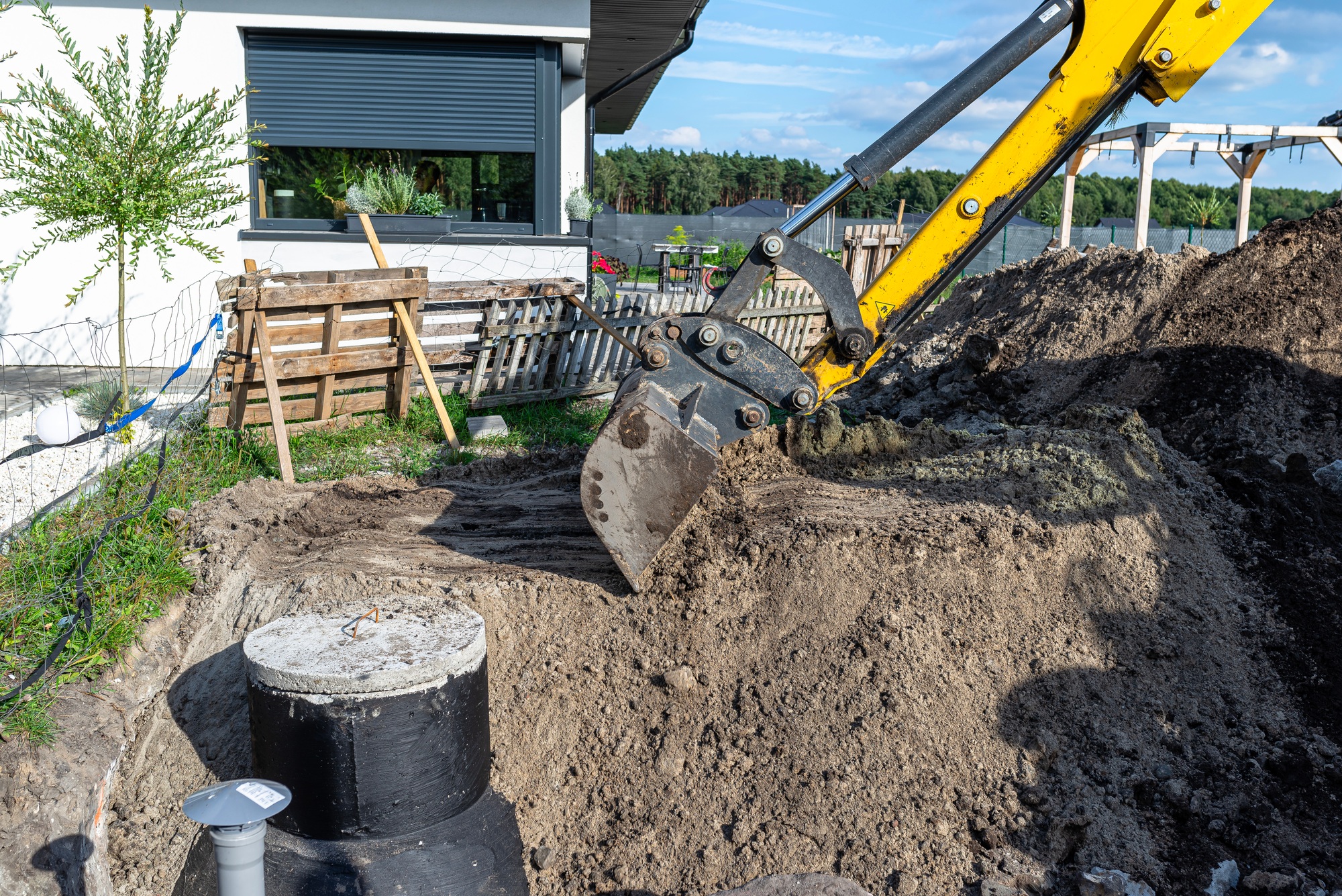 Using an excavator to bury a 10 m3 concrete septic tank located in the garden next to the house.