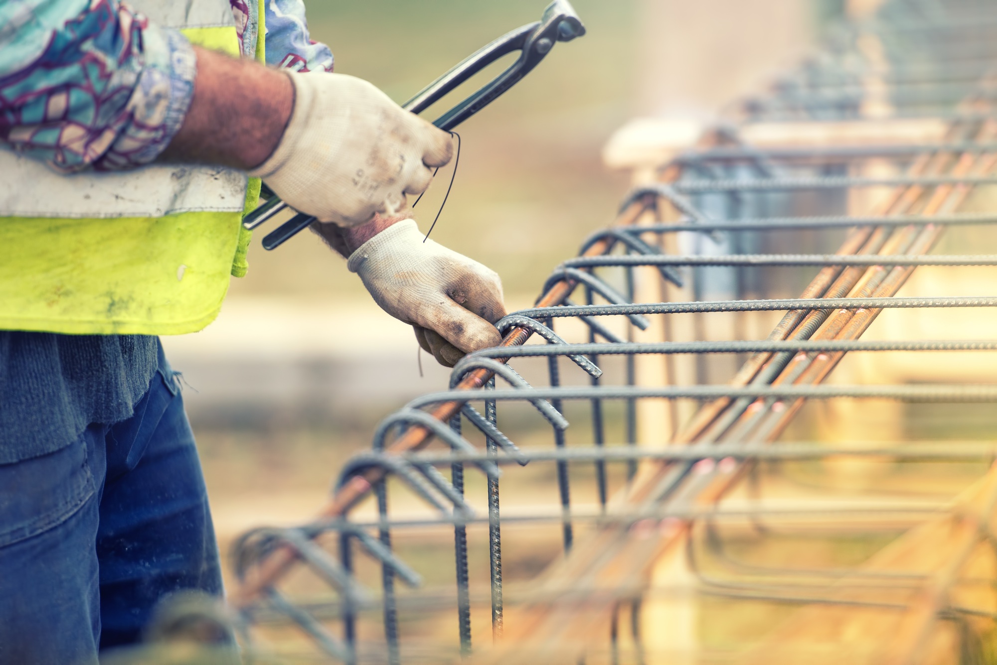 worker hands using steel wire and pliers to secure bars on construction site and preparing