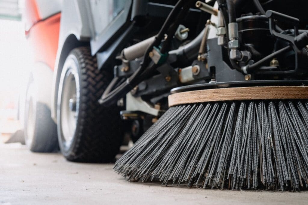 Close-up of a street sweeper brush and wheel on a concrete surface.